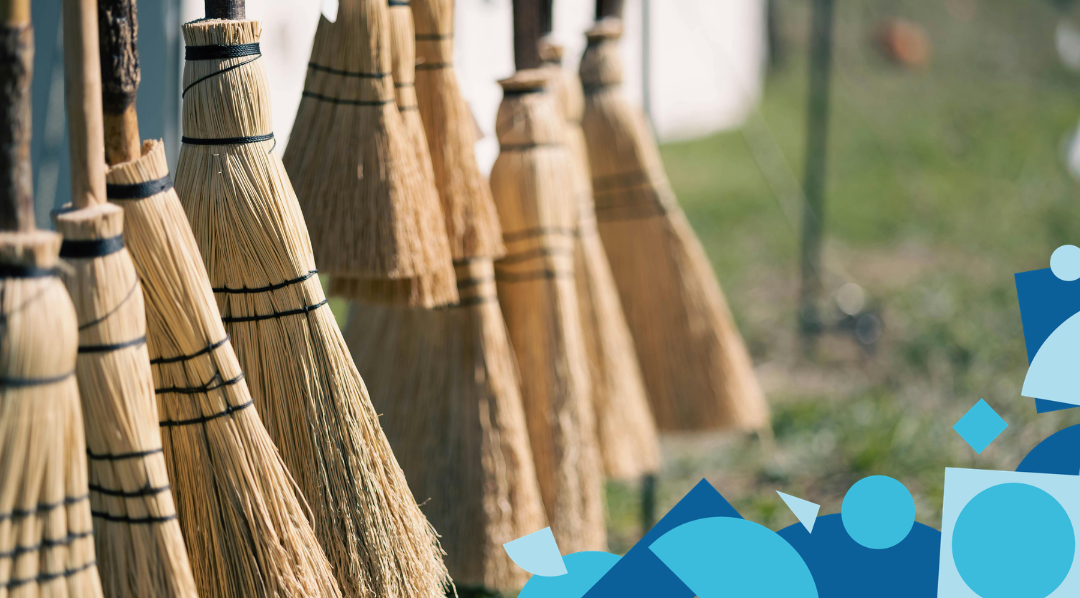 A row of traditional straw broomsticks hanging in a line outdoors in sunlight